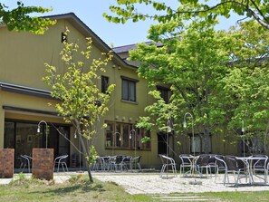 A building with a yellow facade, outdoor seating area with metal chairs, and a tree in the foreground. - Hotel Folkloro Hanamakitowa (Hanamaki)