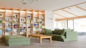 A cozy reading area with bookshelves, a green sofa, and a wooden table. - Hotel Folkloro Hanamaki Towa (Hanamaki)