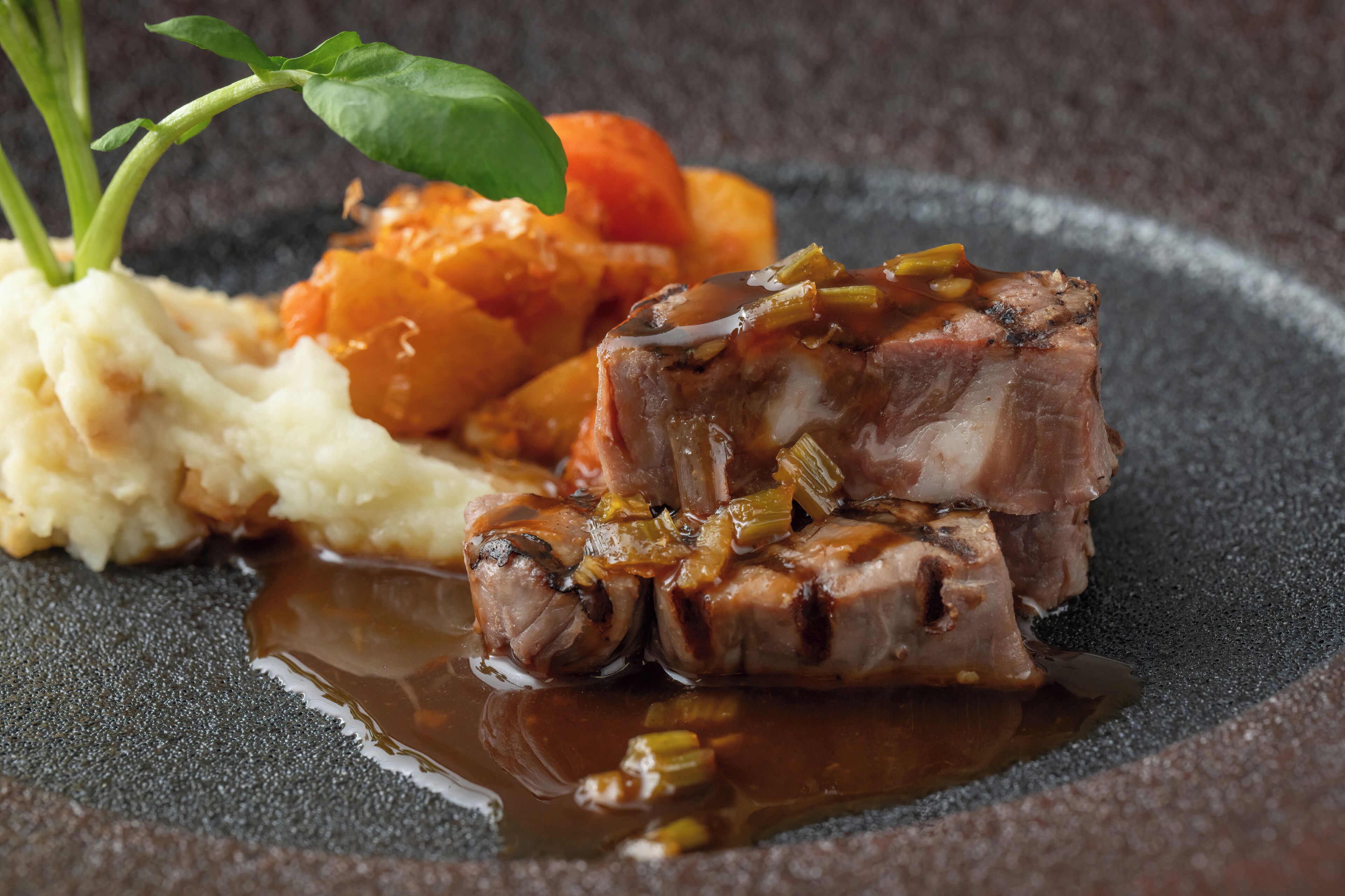 A plate with a piece of meat, mashed potatoes, and roasted vegetables.