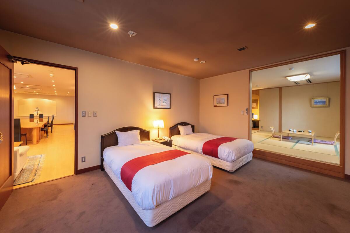 A hotel room with two beds, a desk, and a bathroom visible through an open door.