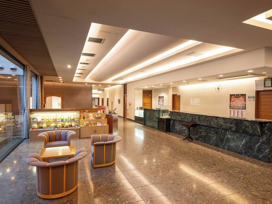 Un lobby moderno de hotel con una recepción, zona de estar y una pared de vidrio que ofrece vistas al exterior.