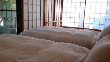 Una habitación con una puerta shoji japonesa tradicional, una cama con ropa blanca y vistas al exterior a través de la pantalla.