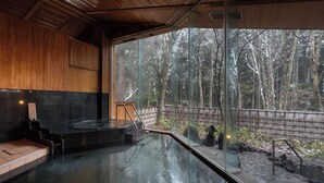A spa area with a glass-enclosed hot tub, wooden interior, and a view of a forested area. - Forest Resort Yamanote Hotel (Daisen)