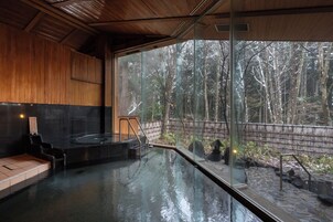 A spa area with a glass-enclosed hot tub, wooden interior, and a view of a forested area.