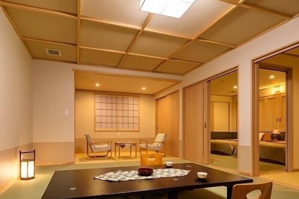 A traditional Japanese-style room with tatami flooring, a low table with a placemat, and a sliding door leading to a bedroom.