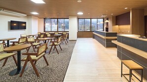 A modern hotel lobby with wooden flooring, round tables, and chairs, a reception desk, and large windows offering a view of the city. - Mukaitaki Ryokan (Fukushima)