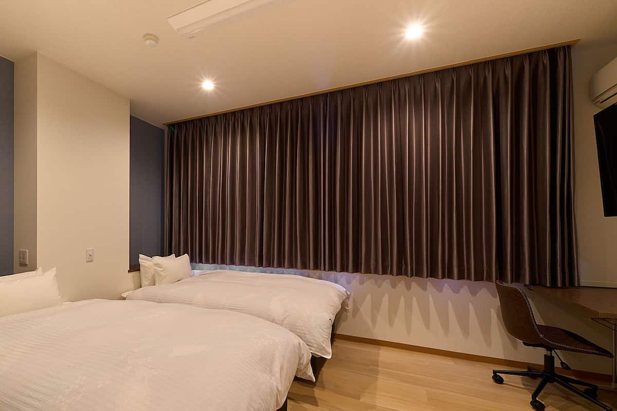 Habitación de hotel con dos camas, un escritorio y un ventanal con cortinas.