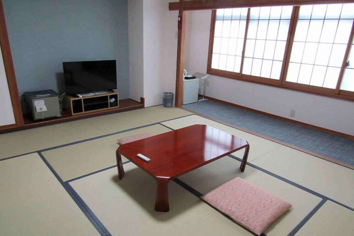 Una habitación con tatami, una mesa de madera, un televisor y un futón.