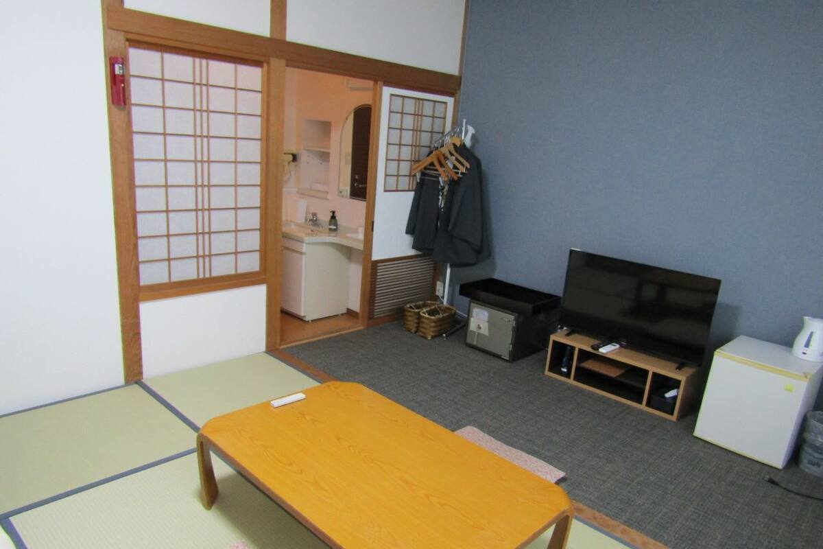 Una habitación japonesa tradicional con suelo de tatami, una mesa de madera baja, un televisor, un refrigerador pequeño y un lavabo.