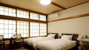 A room with two beds, a desk, and a window with wooden frames. - Mukaitaki Ryokan (Fukushima)
