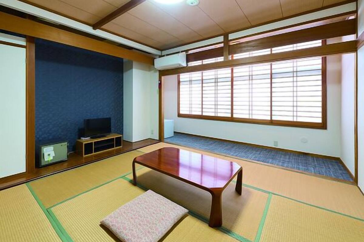 Una habitación japonesa tradicional con suelo de tatami, una mesita baja, un banco y un televisor.