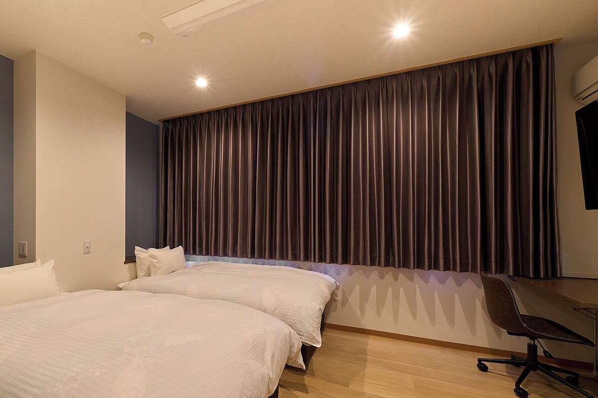 Habitación de hotel con dos camas, un escritorio y un ventanal con cortinas.
