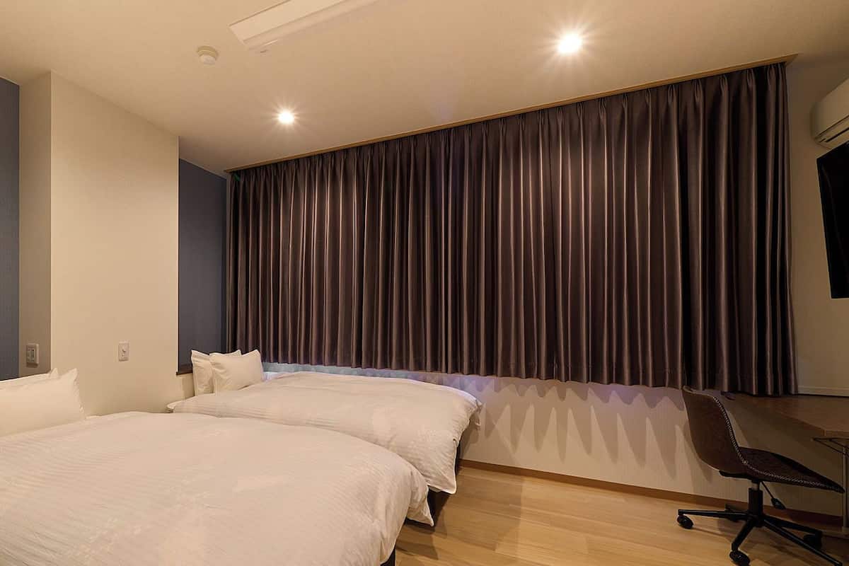 Habitación de hotel con dos camas, un escritorio y un ventanal con cortinas.
