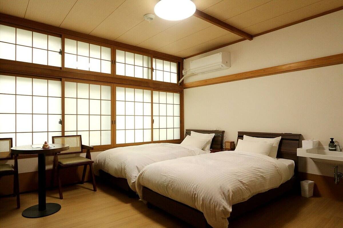 Una habitación con dos camas, un escritorio y una ventana con marcos de madera.