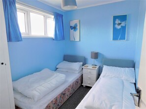 Un dormitorio con dos camas, una mesita de noche con lámpara y una ventana con cortinas azules.