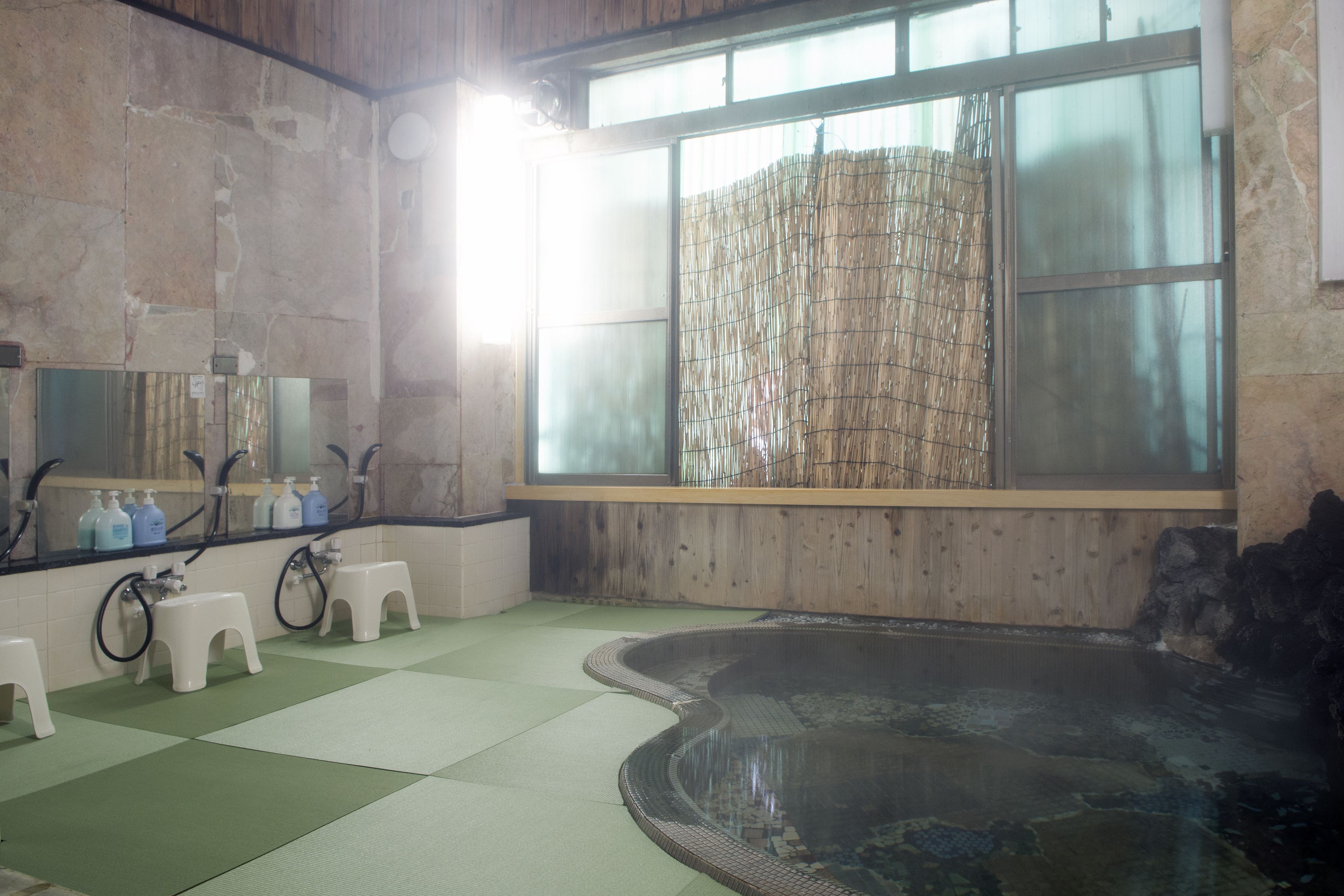 Une salle de bain dotée d’une grande fenêtre, d’une petite piscine et d’un miroir avec des articles de toilette.
