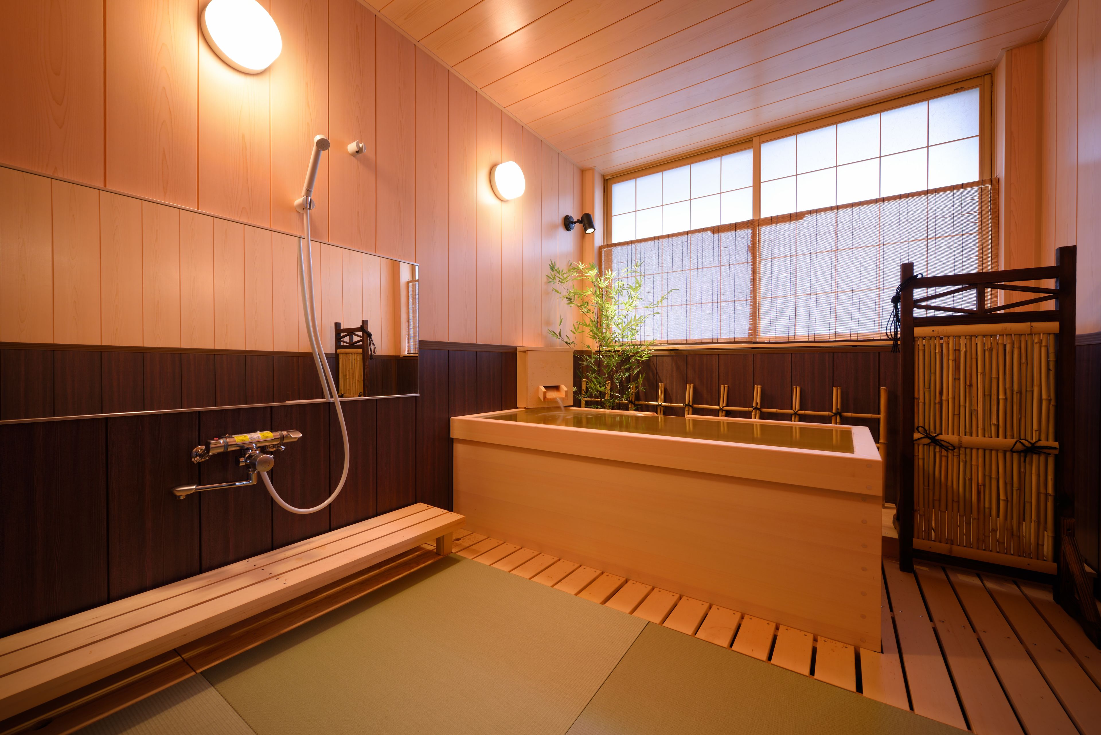 Un baño de estilo japonés tradicional con paredes de madera, una bañera, zona de ducha y una pantalla de bambú.