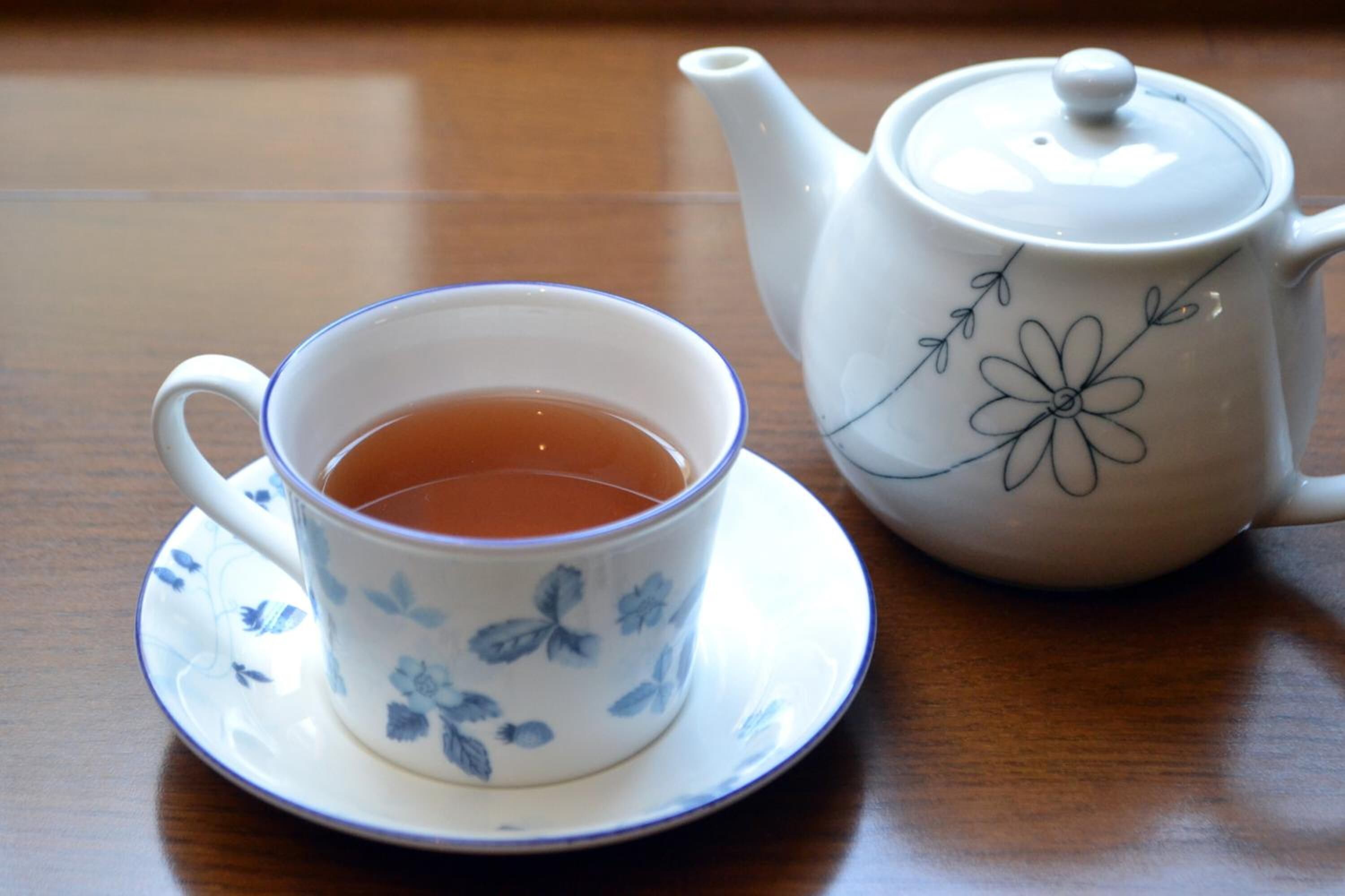 A cup of tea on a saucer and a teapot on a wooden table.