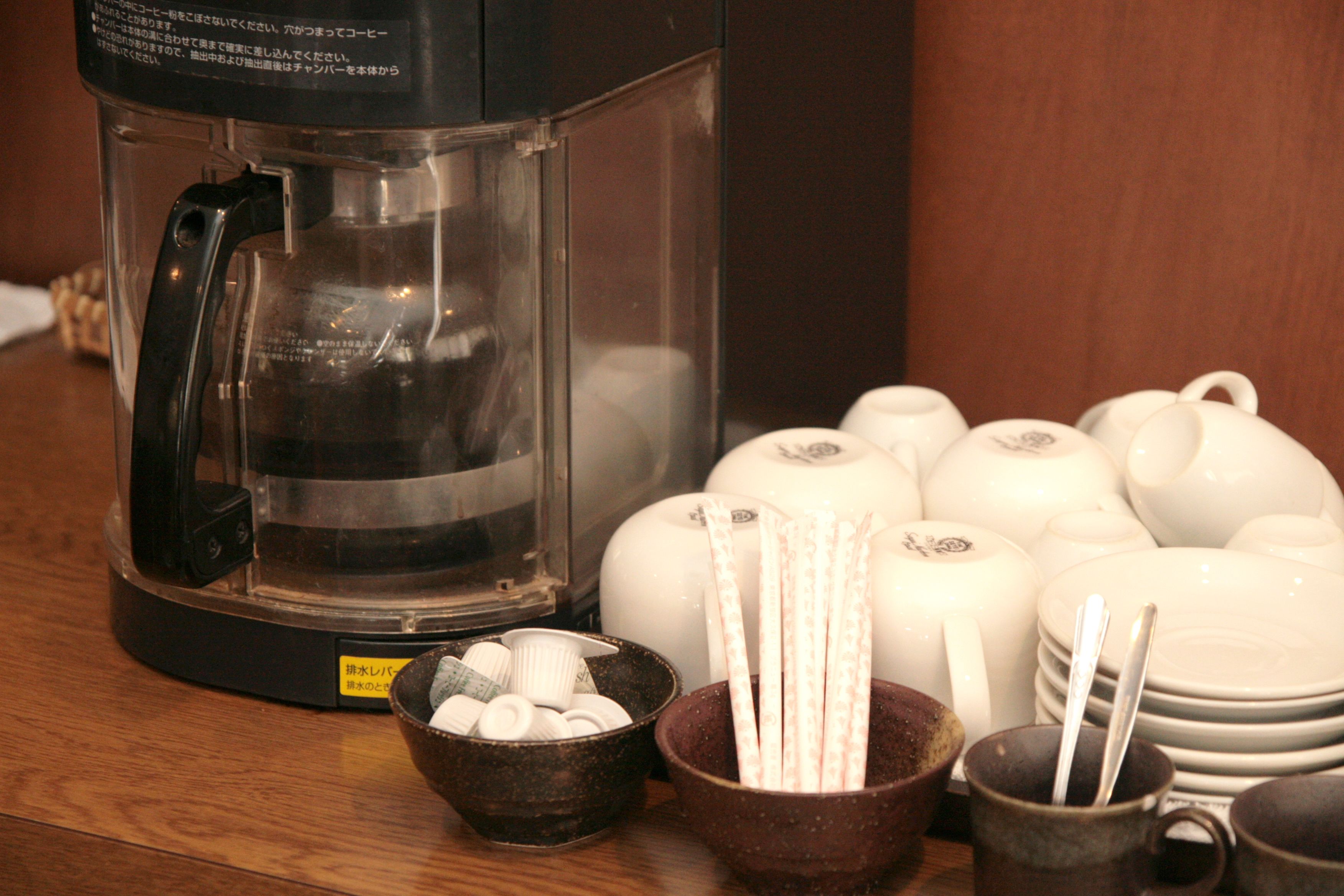 Een koffiezetapparaat, theepotten, bekers en een schaal met rietjes op een houten tafel.