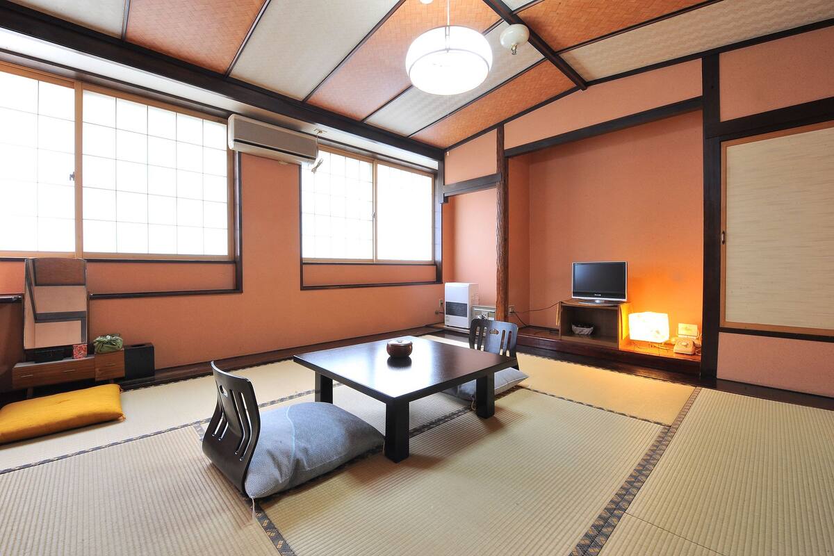 Ett traditionellt japanskt rum med tatamimattor på golvet, ett lågt bord, en kudde, en tv och en värmare.