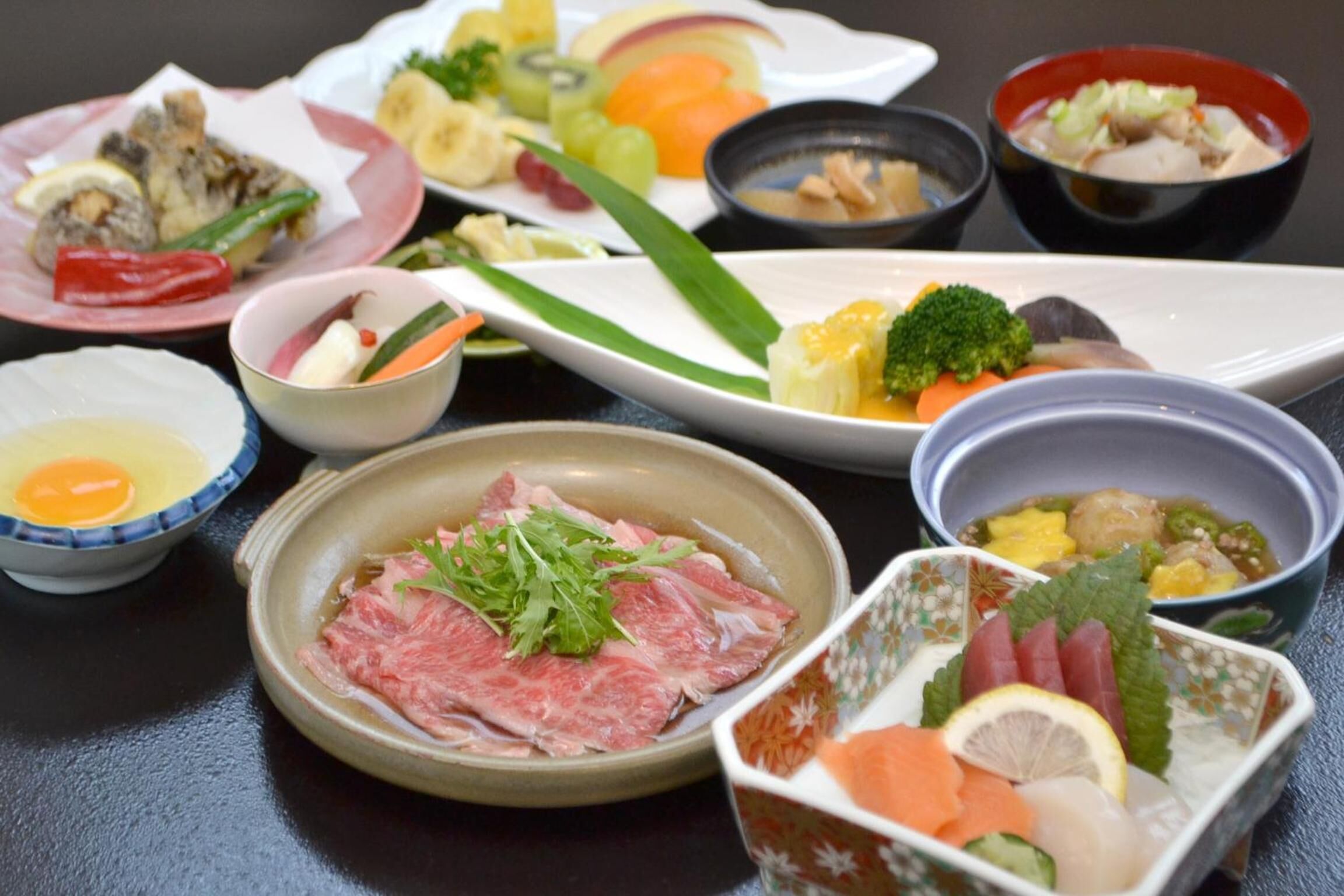 A variety of dishes including sashimi, vegetables, and a bowl of soup.