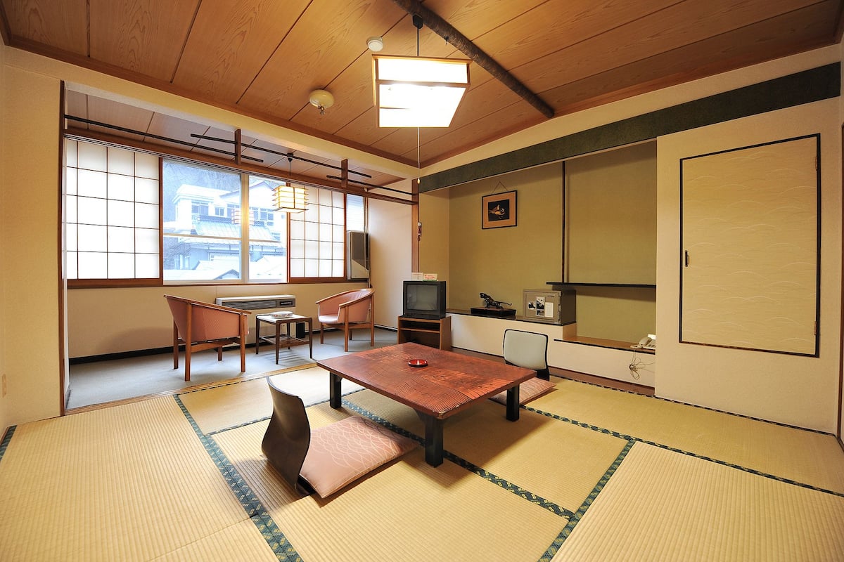 Ett traditionellt japanskt rum med tatamimattor på golvet, ett lågt bord, stolar, en tv och en stor skjutdörr.