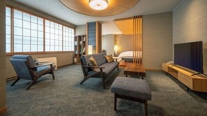 A modern living room with a sofa, two armchairs, a coffee table, a TV, and a bookshelf. - Matsudaya Ryokan (Hanamaki)