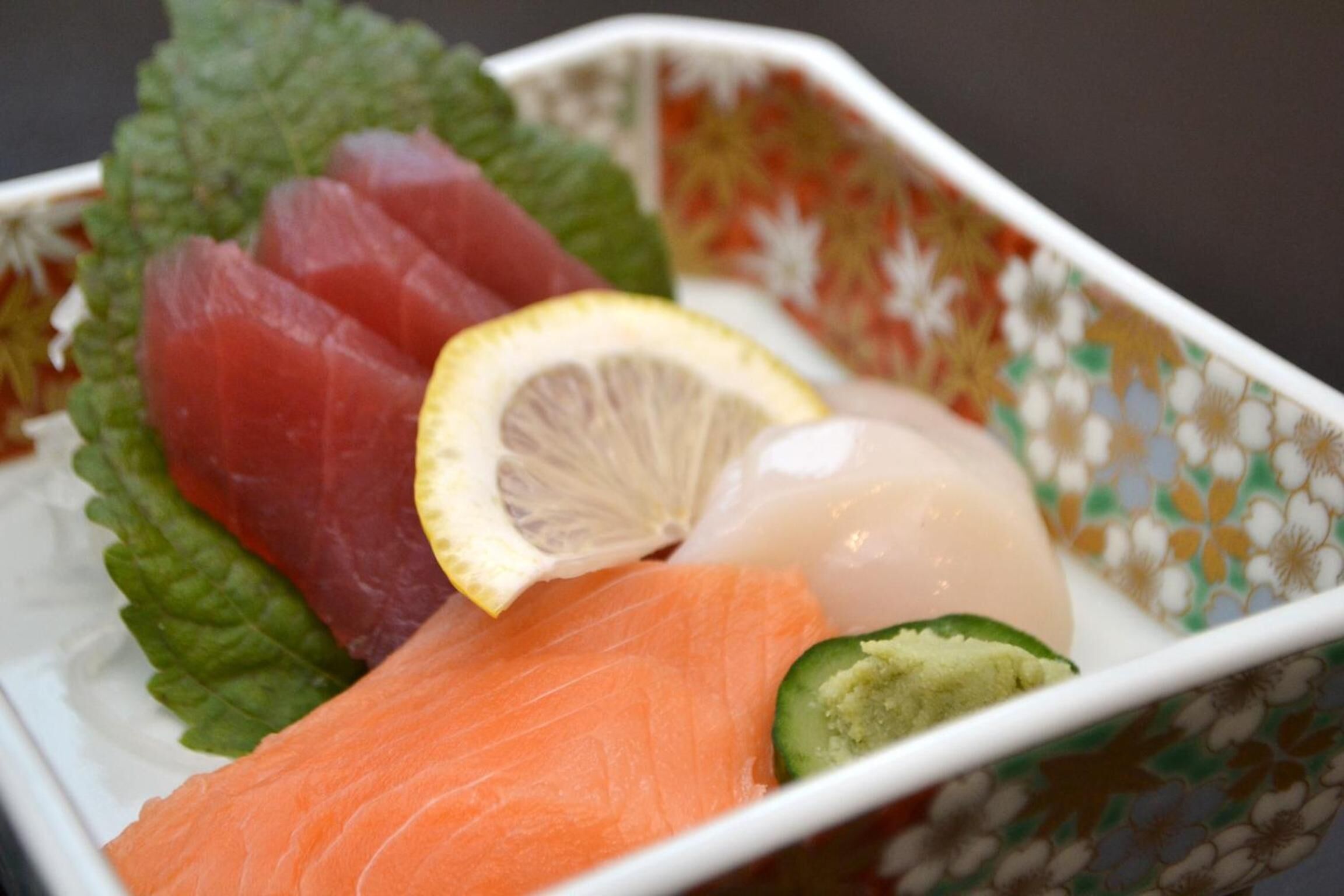 A bowl of sashimi with salmon, tuna, and a lemon slice.