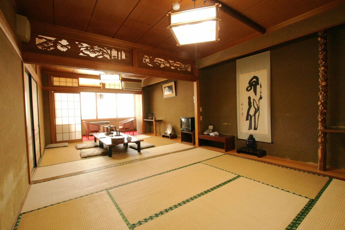 Ett traditionellt japanskt rum med tatamimattor på golvet, ett lågt bord, en tv och en kalligrafisk tavla på väggen.
