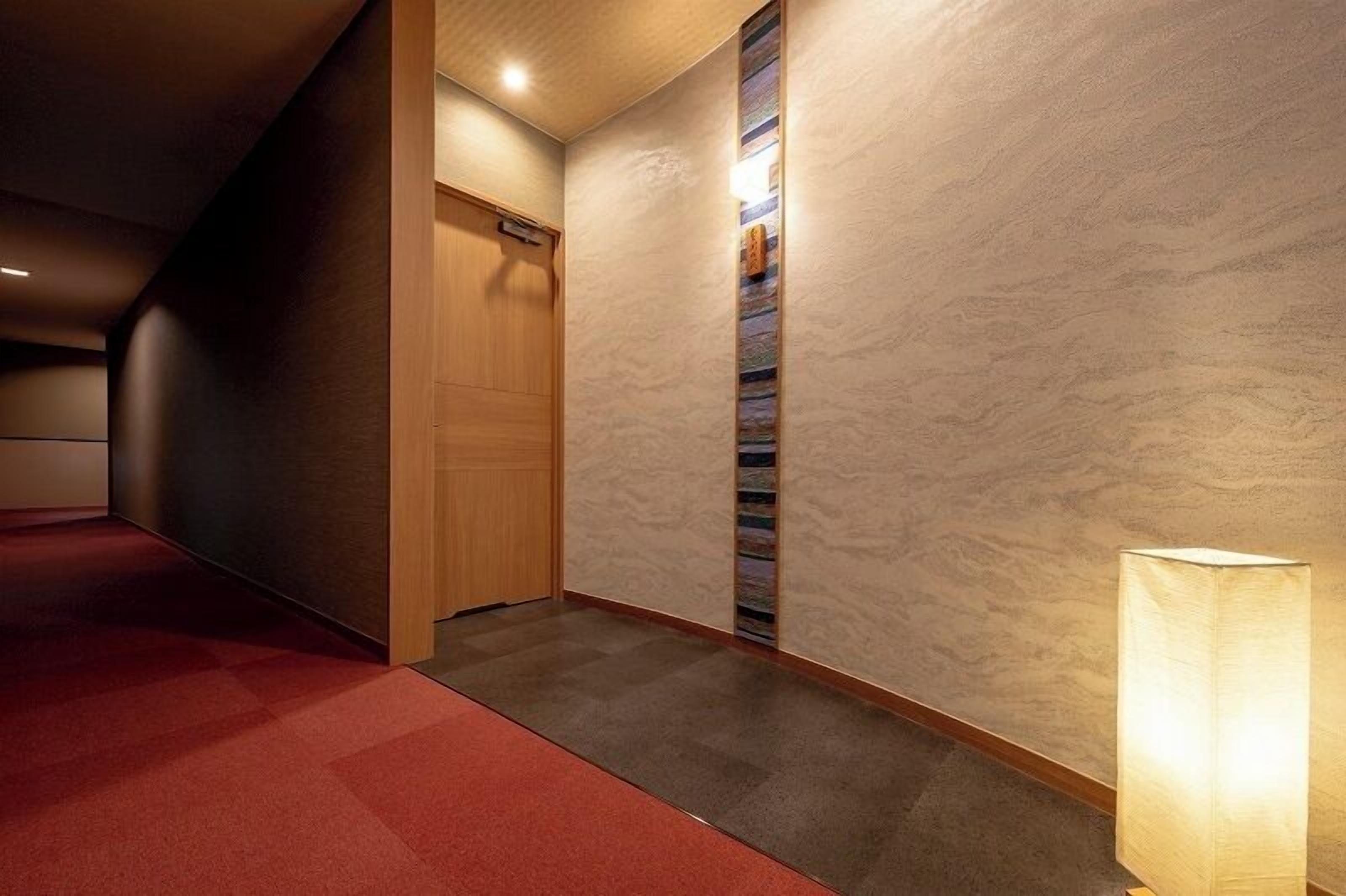 A corridor with a red carpet, a wooden door, and a wall with a textured pattern.