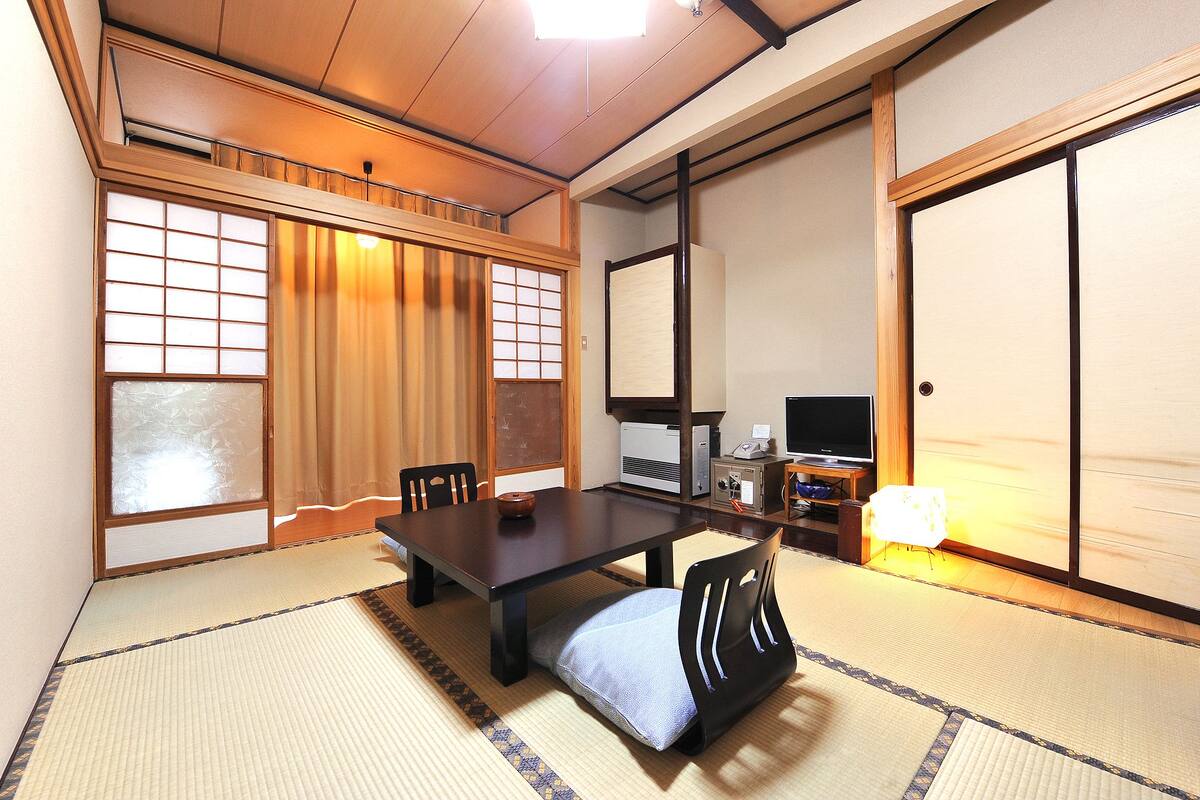 Ett traditionellt japanskt rum med tatamimattor på golvet, ett lågt bord, stolar, en tv och skjutdörrar.