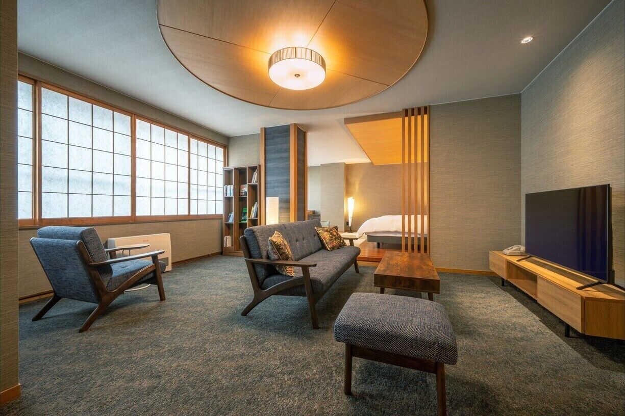 A modern living room with a sofa, chairs, a coffee table, a TV, and a bookshelf.