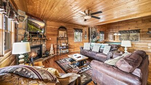 A cozy log cabin interior with a fireplace, leather furniture, and a stone fireplace surround. - Mountain Views & FREE Attraction Tickets (Gatlinburg)