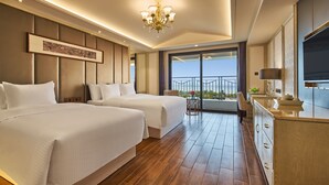 Quarto de hotel com duas camas, um lustre, uma janela grande e uma varanda com vista.