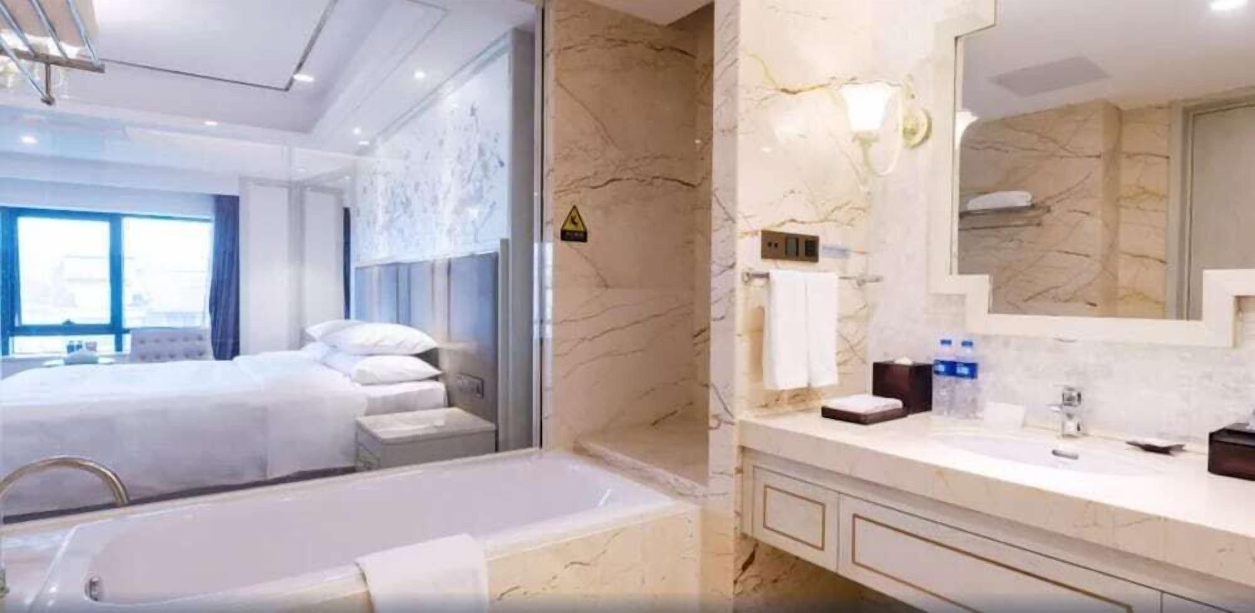 A modern hotel room with a large bed, a separate bathroom with a bathtub, and a marble wall.