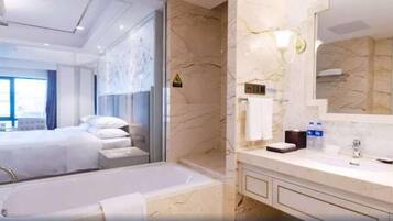 A modern hotel room with a large bed, a separate bathroom with a bathtub, and a marble wall.