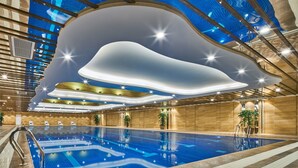 Uma piscina interior com design moderno no teto, área de piscina bem iluminada e plantas em vasos.