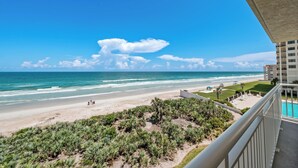 A beachfront view from a balcony overlooking a sandy beach, ocean, and a pool area. - Direct oceanfront southern corner 2/2 condo with large wrap-around balcony and heated pool (New Smyrna Beach)