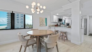 A modern kitchen with white cabinets, a stainless steel refrigerator, and a dining area with wicker chairs and a round table. - Direct oceanfront southern corner 2/2 condo with large wrap-around balcony and heated pool (New Smyrna Beach)