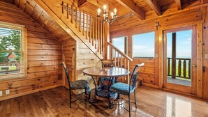 A wooden cabin interior with a dining area, a staircase, and large windows.