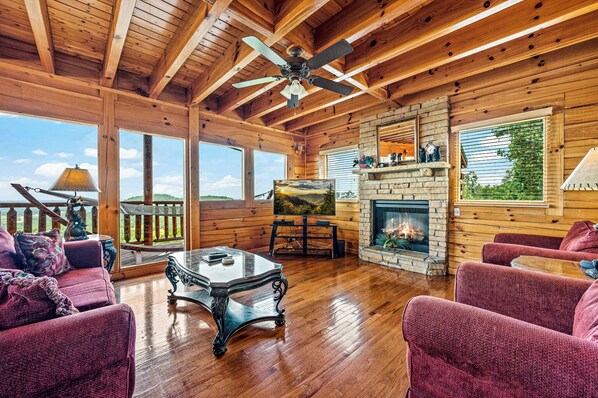 A log cabin interior with a fireplace, wooden furniture, and large windows.