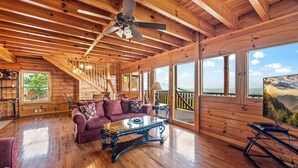 A spacious wooden cabin with a large living area, a staircase, and a scenic view through the windows.