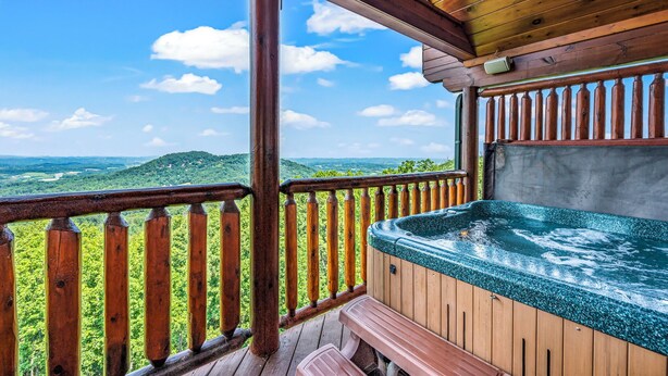A wooden deck with a hot tub and a view of green hills.