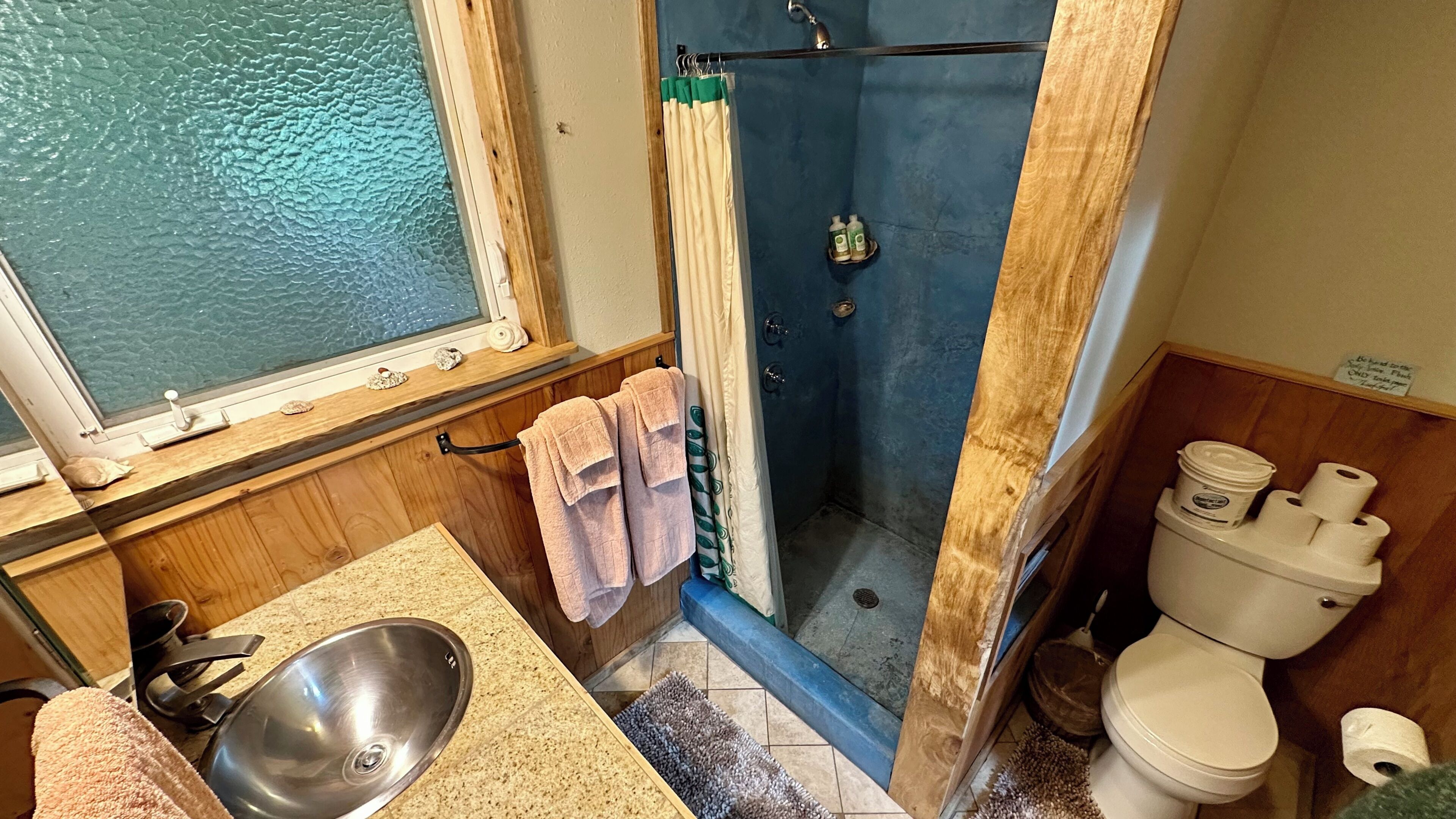 A bathroom with a shower, toilet, sink, and a window.