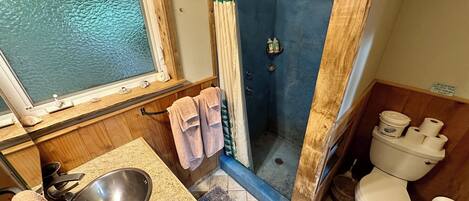 A bathroom with a shower, toilet, sink, and a window.