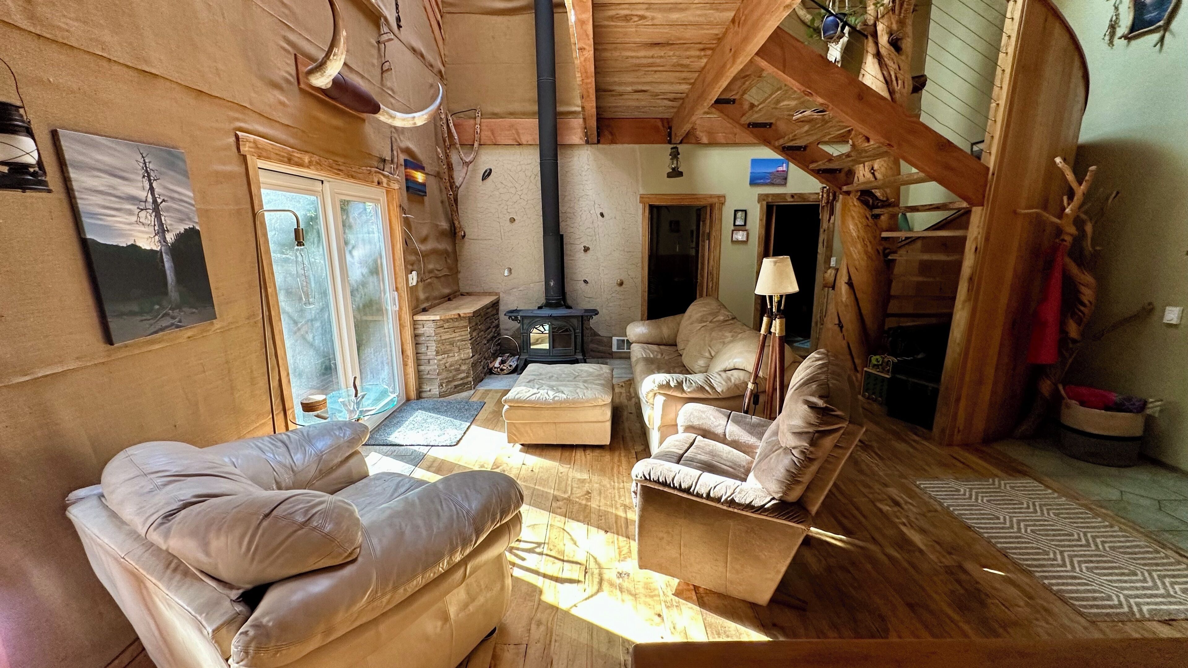 A rustic cabin interior with a stone fireplace, leather sofas, and a wooden ceiling.