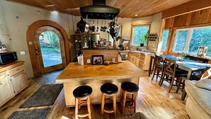 Una cocina con una isla central, taburetes de madera y vistas a través de un arco.