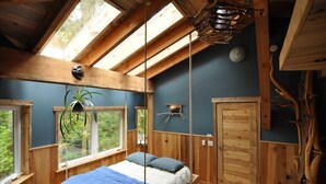 Un dormitorio con cama, ventanas, una planta colgante y techo de madera.