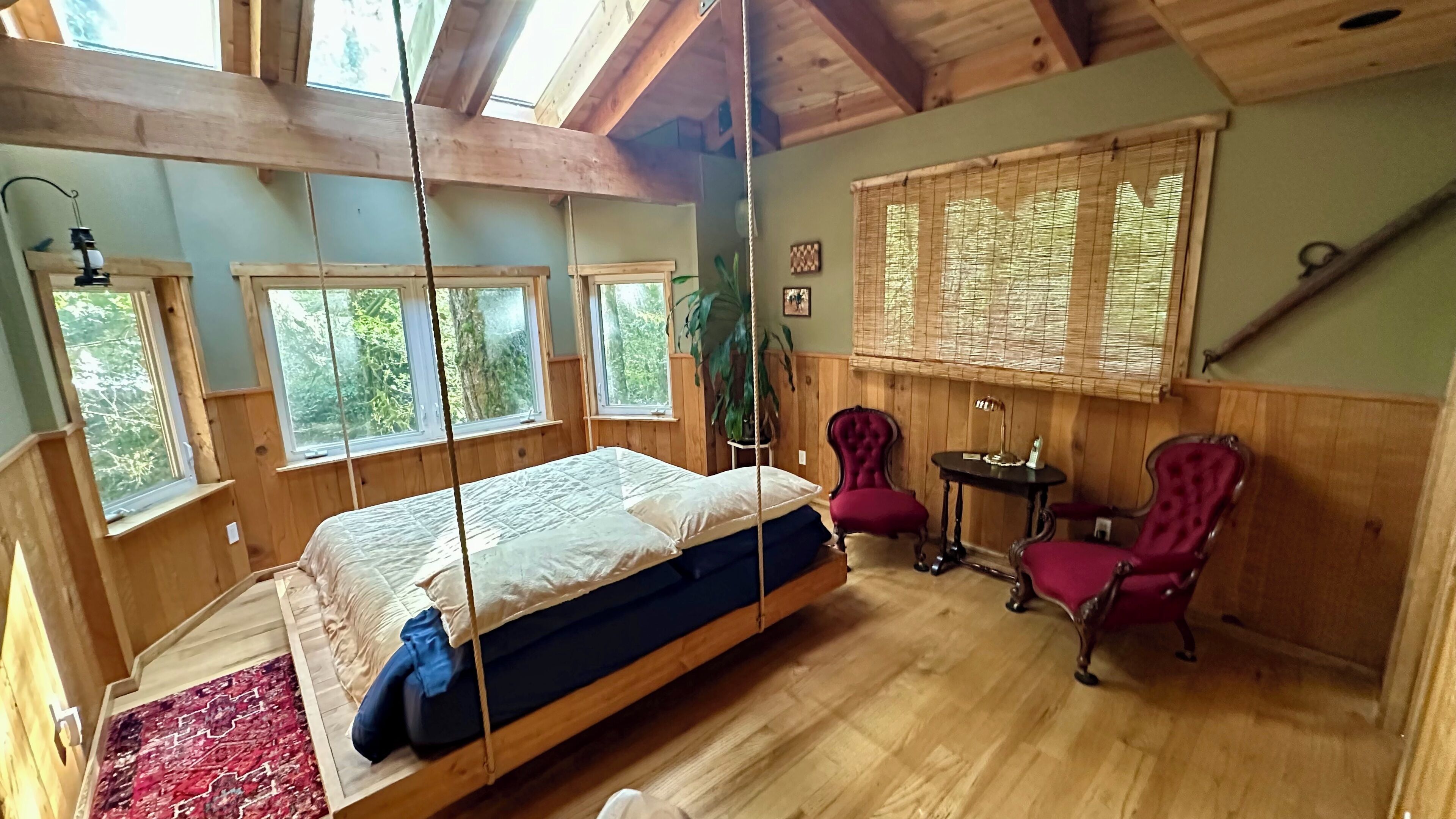 A wooden room with a bed, two chairs, a table, and large windows.