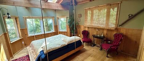 A wooden room with a bed, two chairs, a table, and large windows.